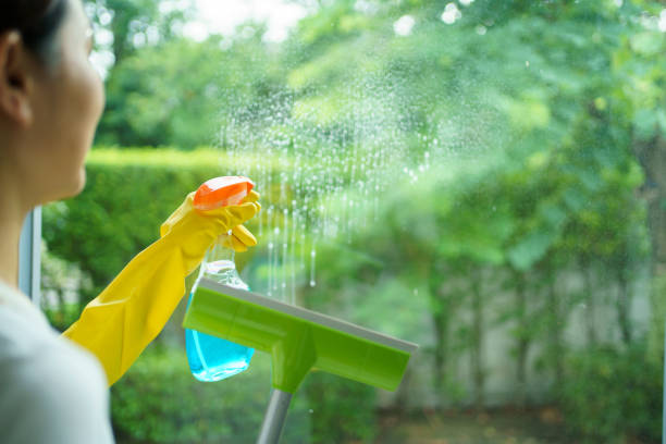 Close-up, side view of woman cleaning a window with a spray bottle and rubber squeegee.