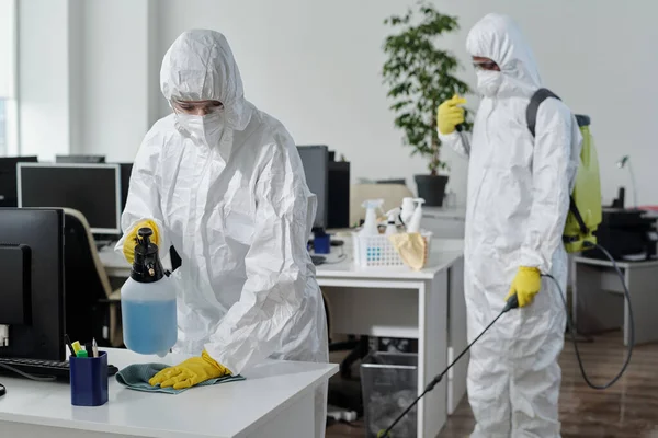 Disinfection service company staff in protective suit carrying out their work in spacious office