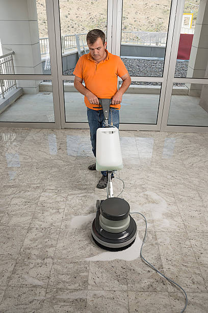 Worker wearing uniform cleaning marble floor with buffer machine.