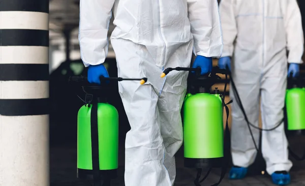 Unrecognisable people in protective gear holding disinfectant sprays.