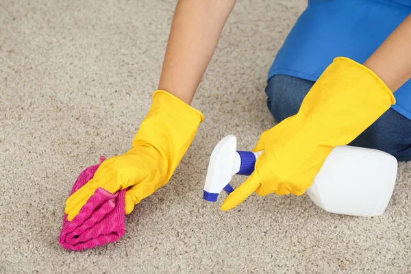 Woman cleaning carpet at home with cloth and spray bottle close up