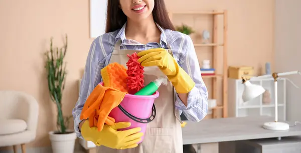 Cropped shot of a woman holding cleaning supplies in a living room background.