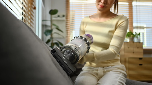 Cropped shot of young woman using handheld cordless vacuum cleaner to vacuuming and cleaning the dust on couch