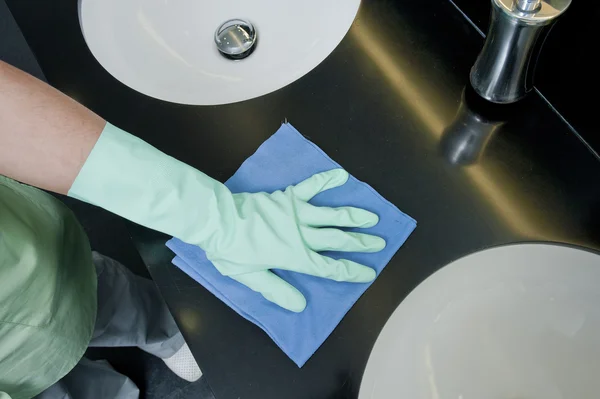 Hand in rubber glove wiping countertop in the bathroom.