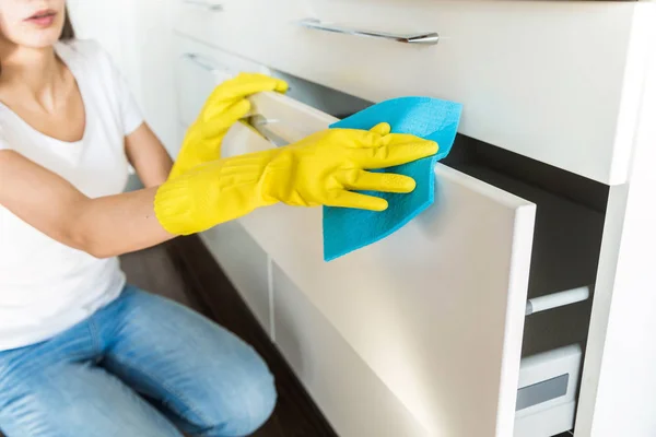 Woman in yellow gloves cleaning inside cabinet.