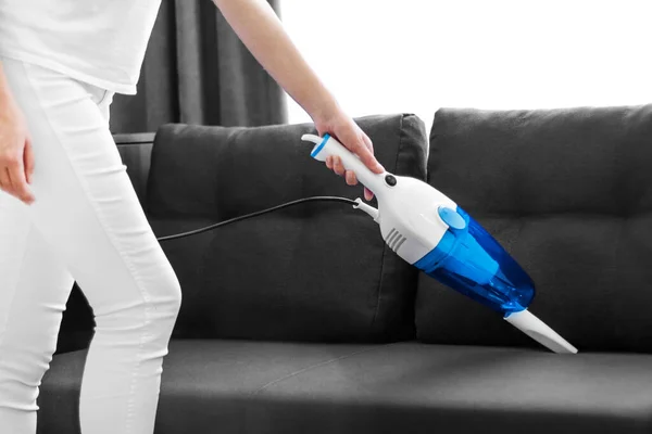 Woman cleans the sofa with a hand vacuum cleaner.