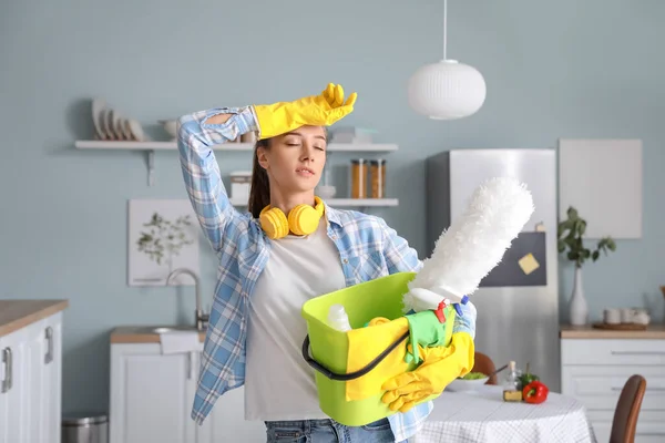 A tired woman in yellow gloves with cleaning supplies in the kitchen.