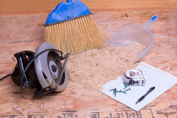 Handheld circular saw with sawdust, brush and pan lying on the floor with a tape measure, pen and nails on paper, concept of mess after renovation