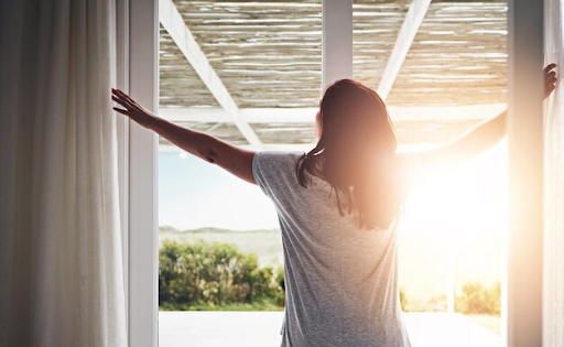 Back view of a woman opening a window to improve ventilation and let fresh air in.